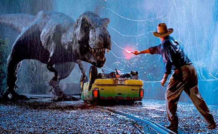 A scene from the film Jurassic Park. A T Rex stands near a car in a thunderstorm, while Alan Grant waves a light.